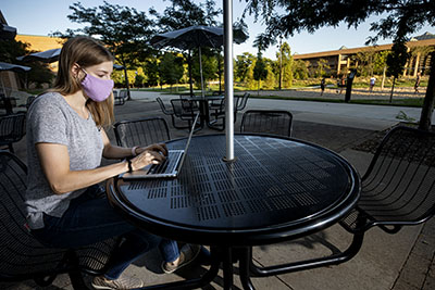 woman wearing facemask working on a laptop computer at an outdoor table